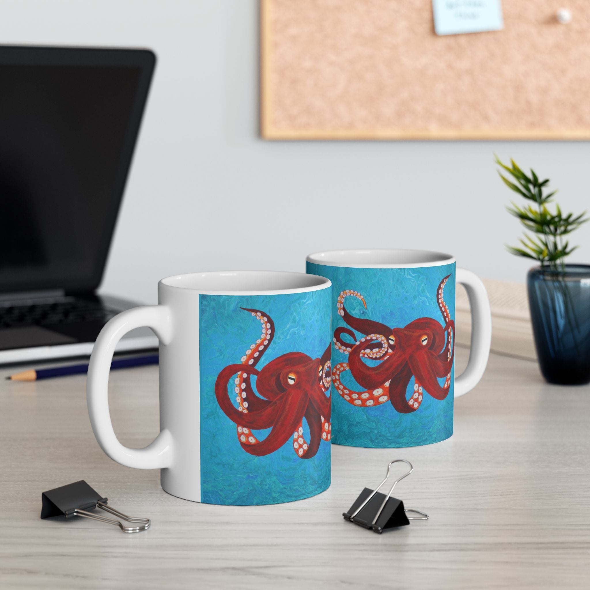 2 coffee cups on desk with image of red octopus swimming in turquoise sea on both