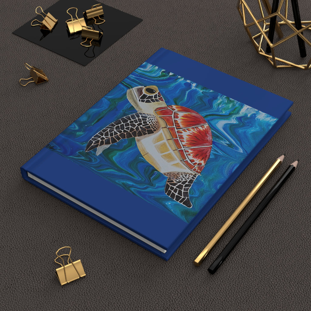 Blue notebook with a turtle illustration on a dark surface with stationery items.