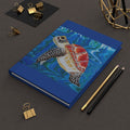 Blue notebook with a turtle illustration on a dark surface with stationery items.