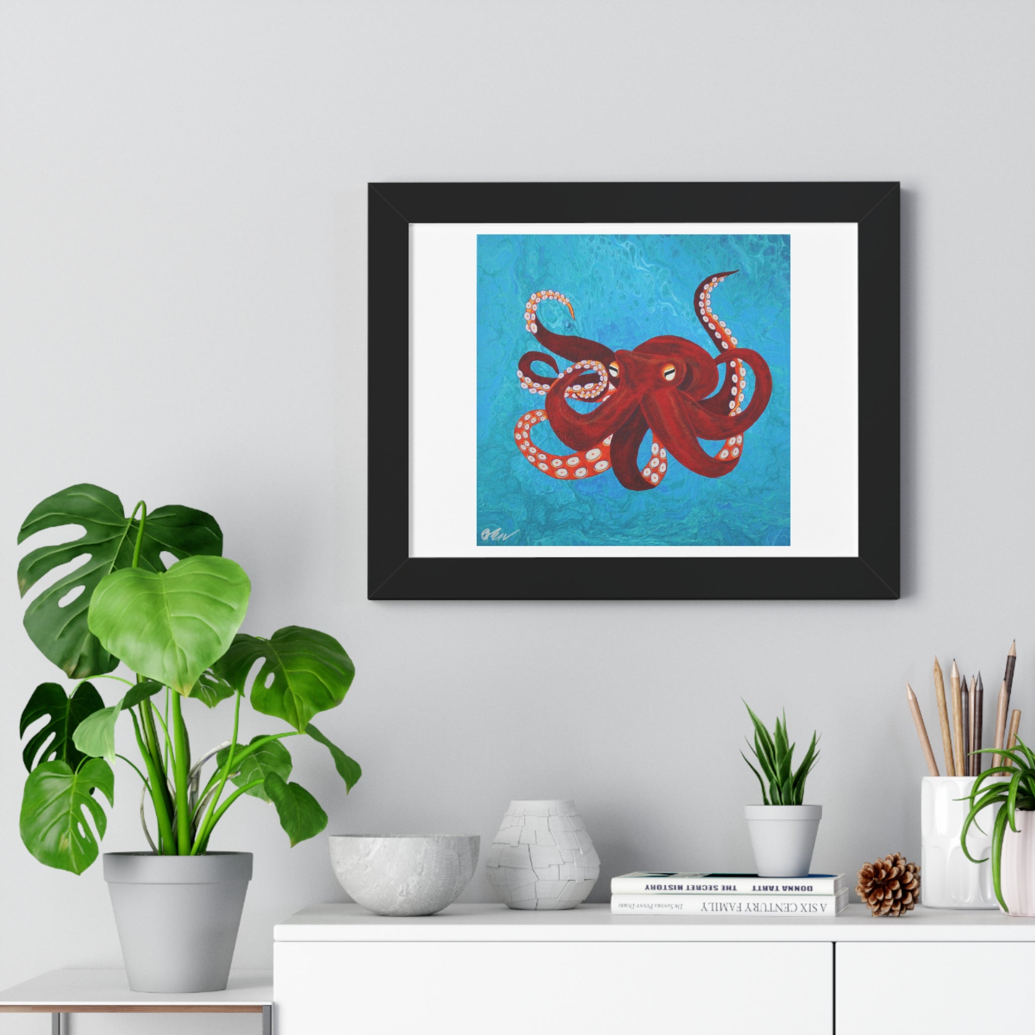 Framed artwork of a red octopus on a blue background, displayed in a home setting with plants and decor.