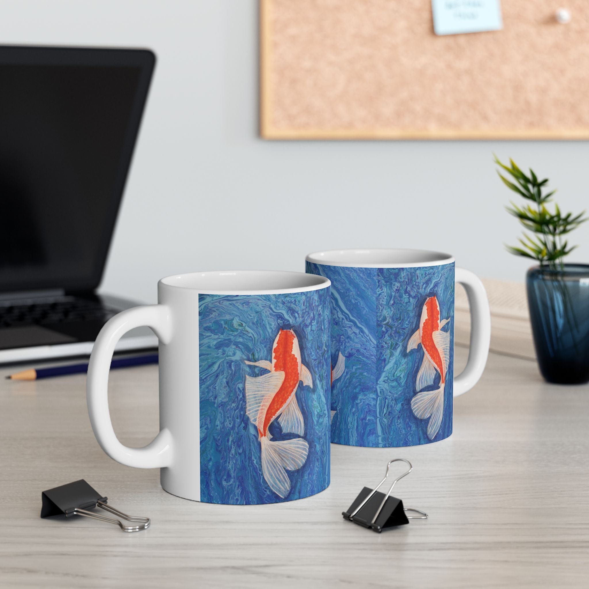 Two mugs with koi fish design on a desk with office items.