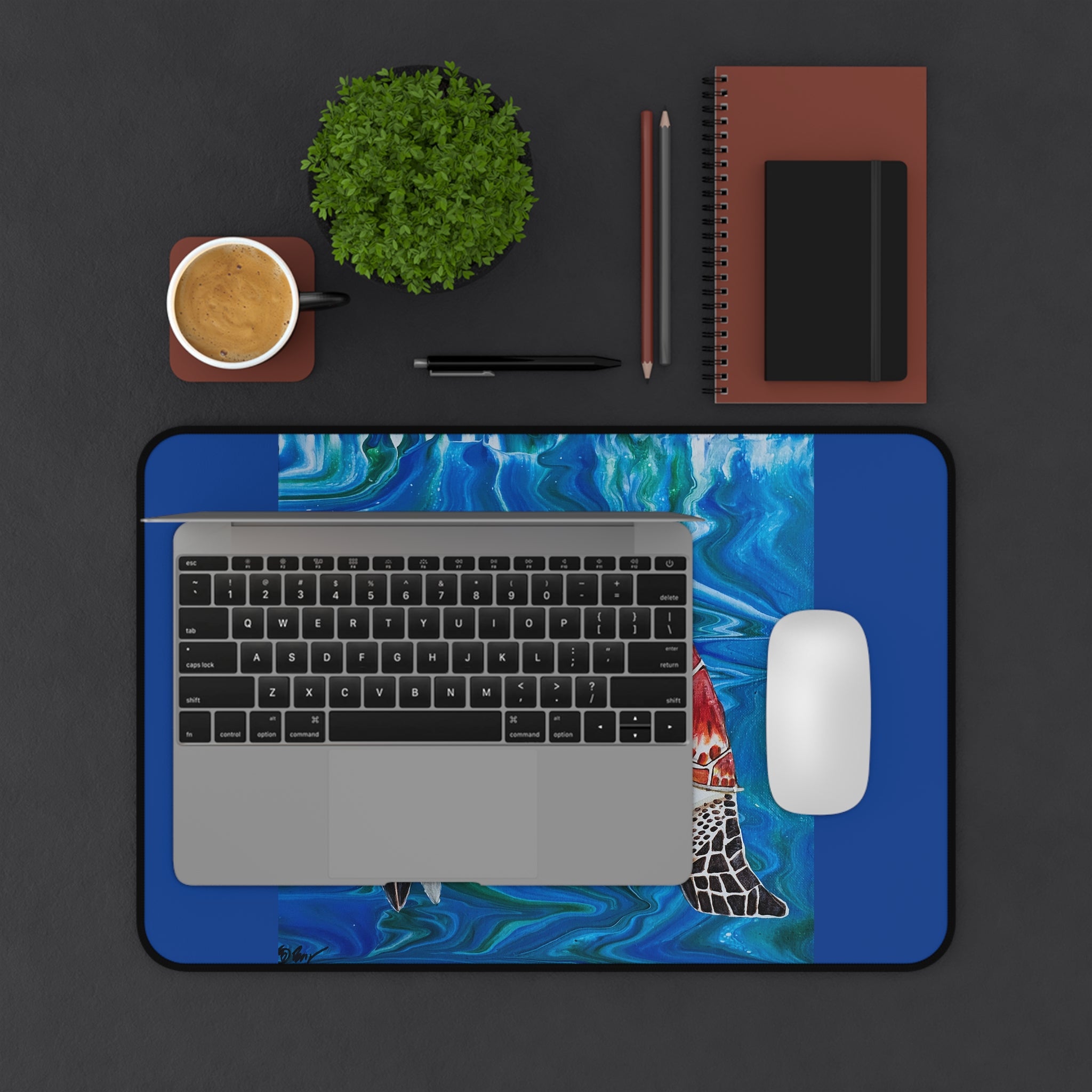 Laptop on a blue desk pad with a fish design, surrounded by office items on a dark surface.