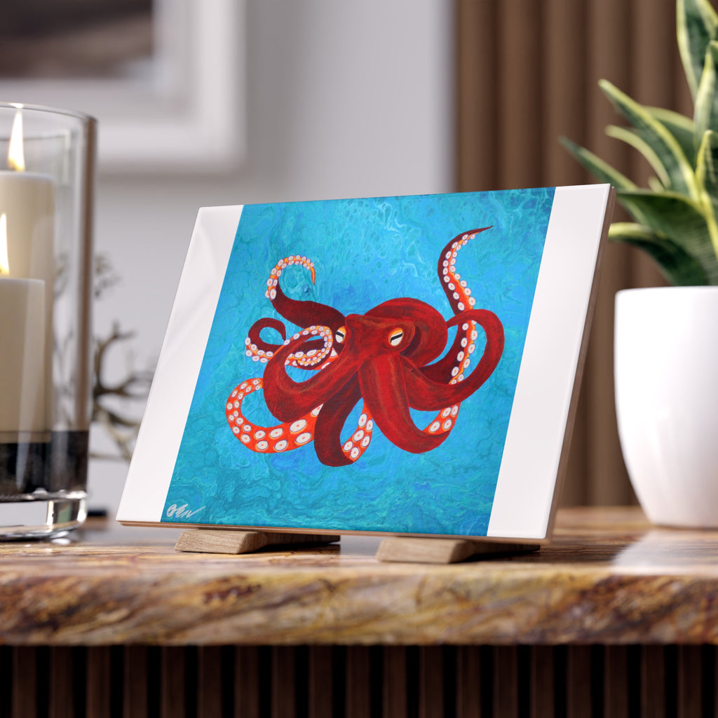 Tile with a red octopus design on a blue background, placed on a wooden surface.