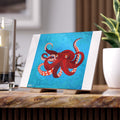 Tile with a red octopus design on a blue background, placed on a wooden surface.