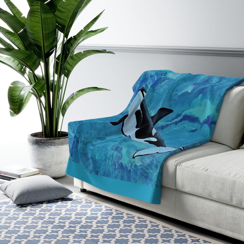 Orca whale blanket draped over a couch in a living room setting with a plant and rug.