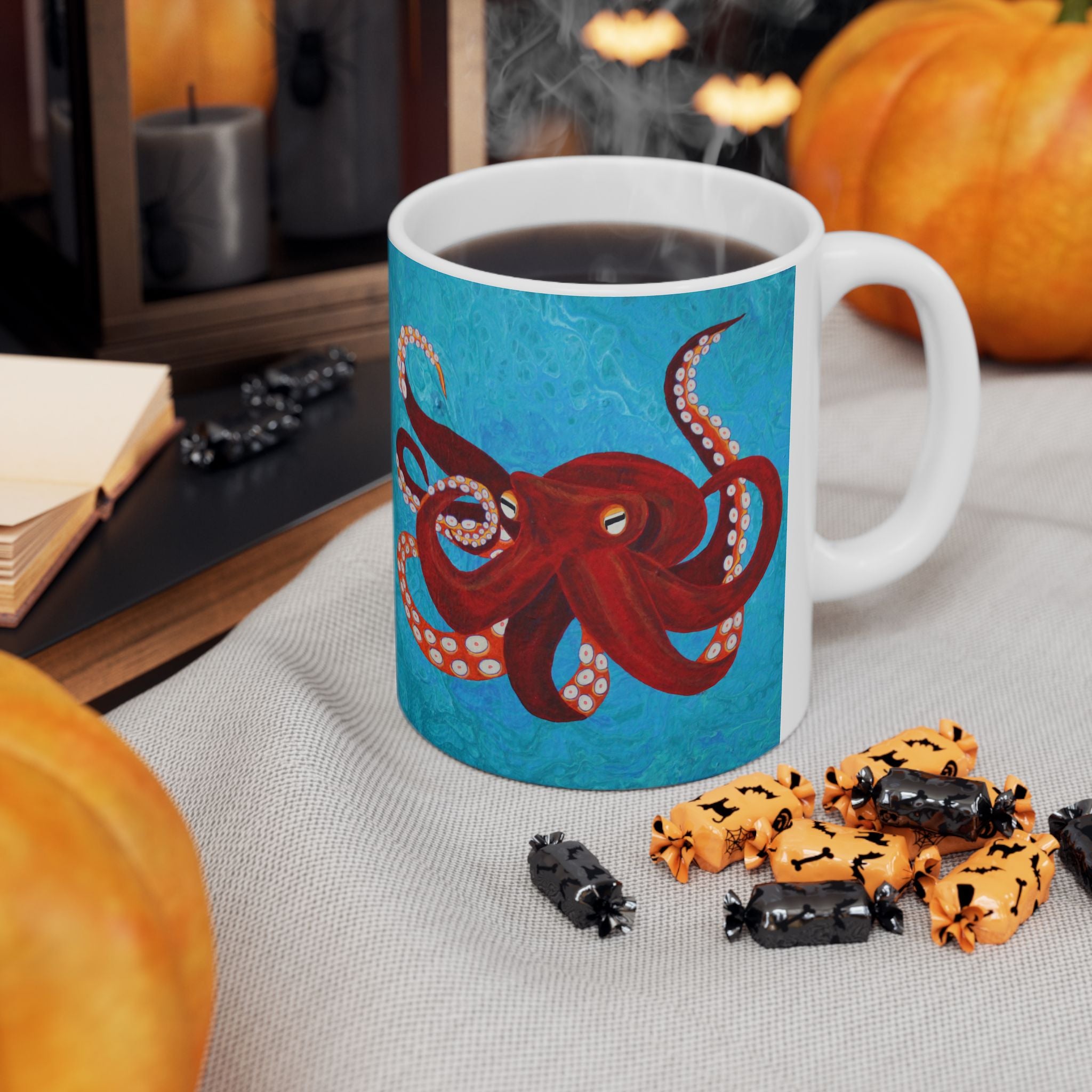 Mug with a red octopus design on a table with Halloween-themed treats and pumpkins.