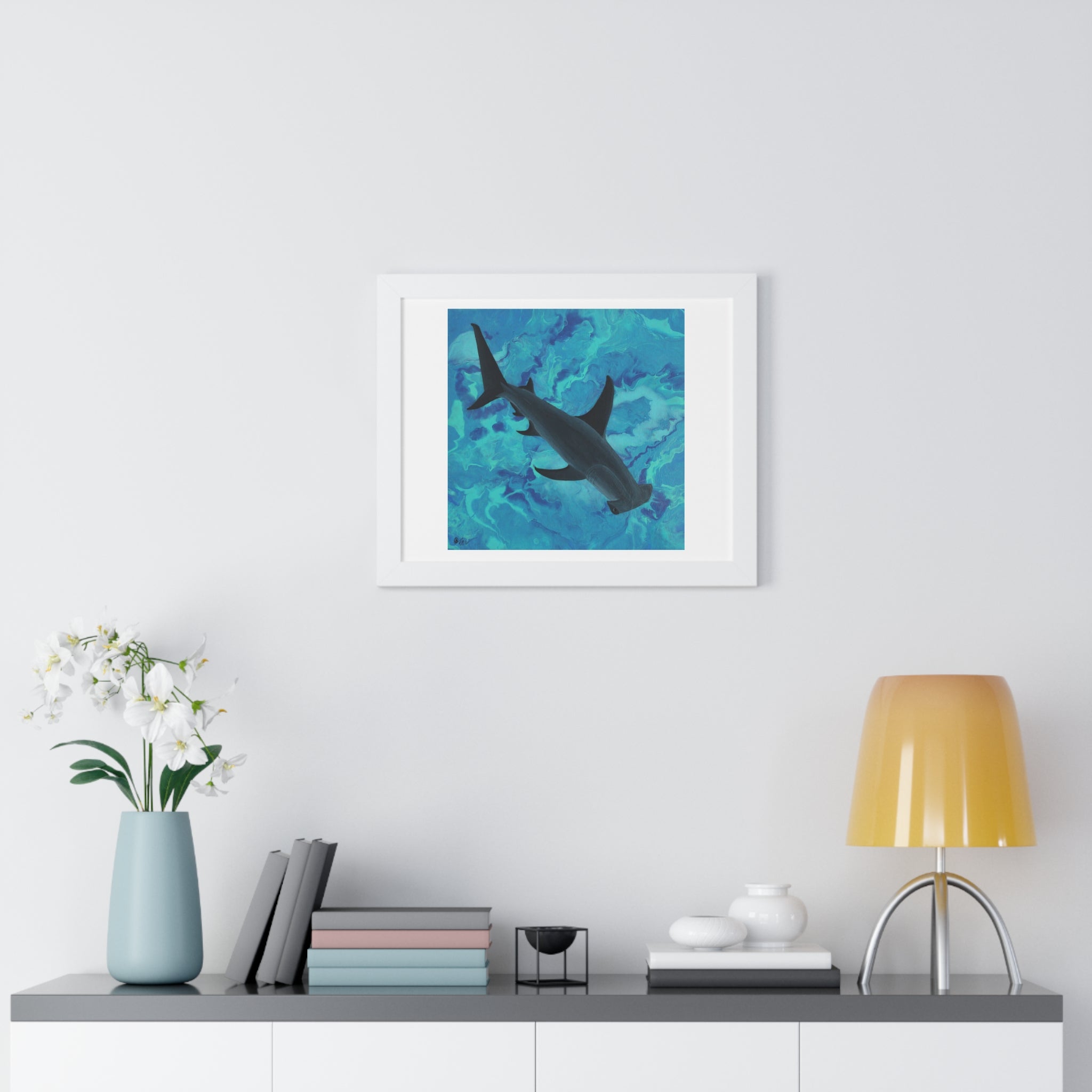 Framed artwork of a shark in water on a wall above a shelf with decor items.