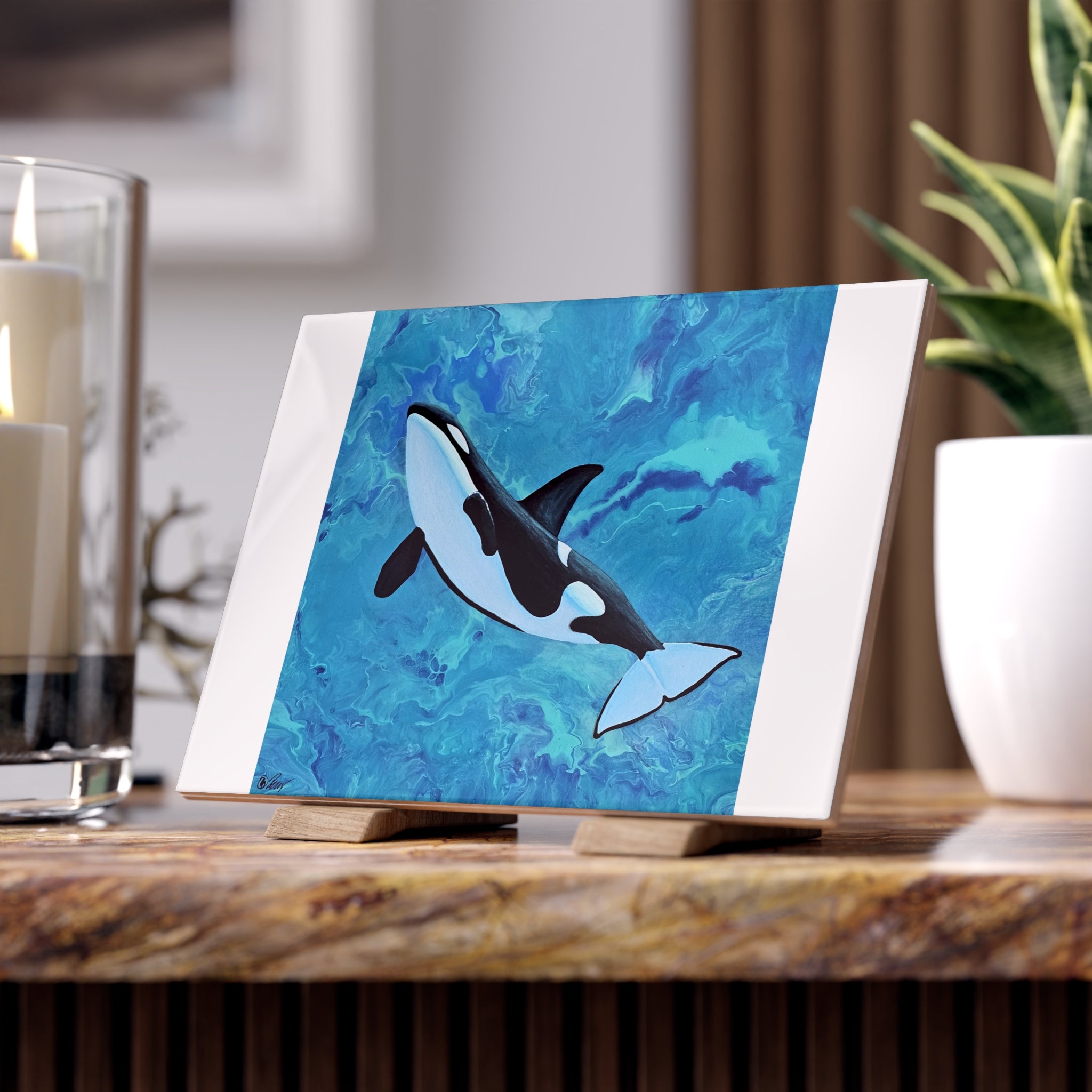 Orca whale painting on a stand with candles and a plant in the background tile