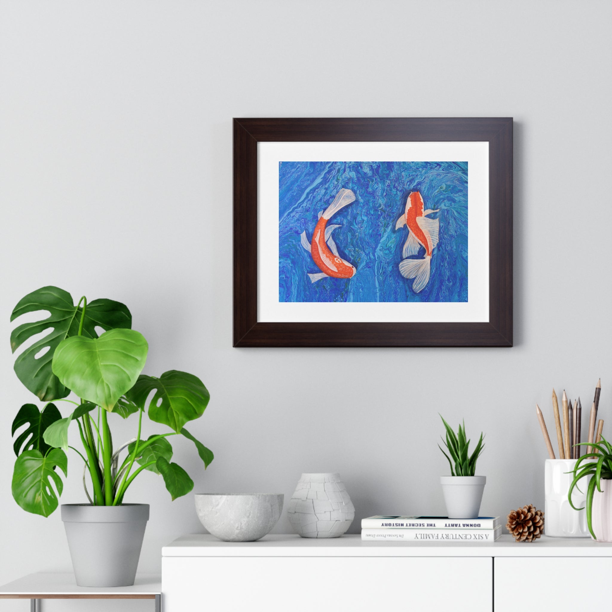 Framed artwork of two fish on a wall above a white cabinet with decorative items.