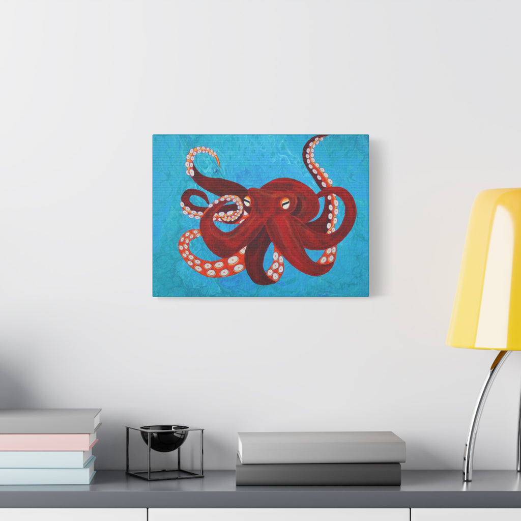 Canvas print of a red octopus on a blue background hanging above a desk with books and a lamp.