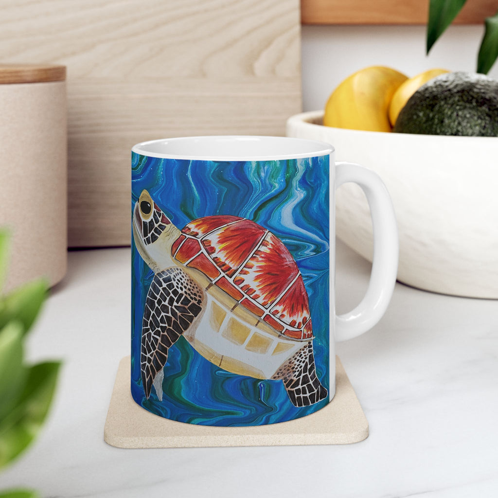 Mug with a turtle design on a coaster, placed on a surface with a plant and container in the background.