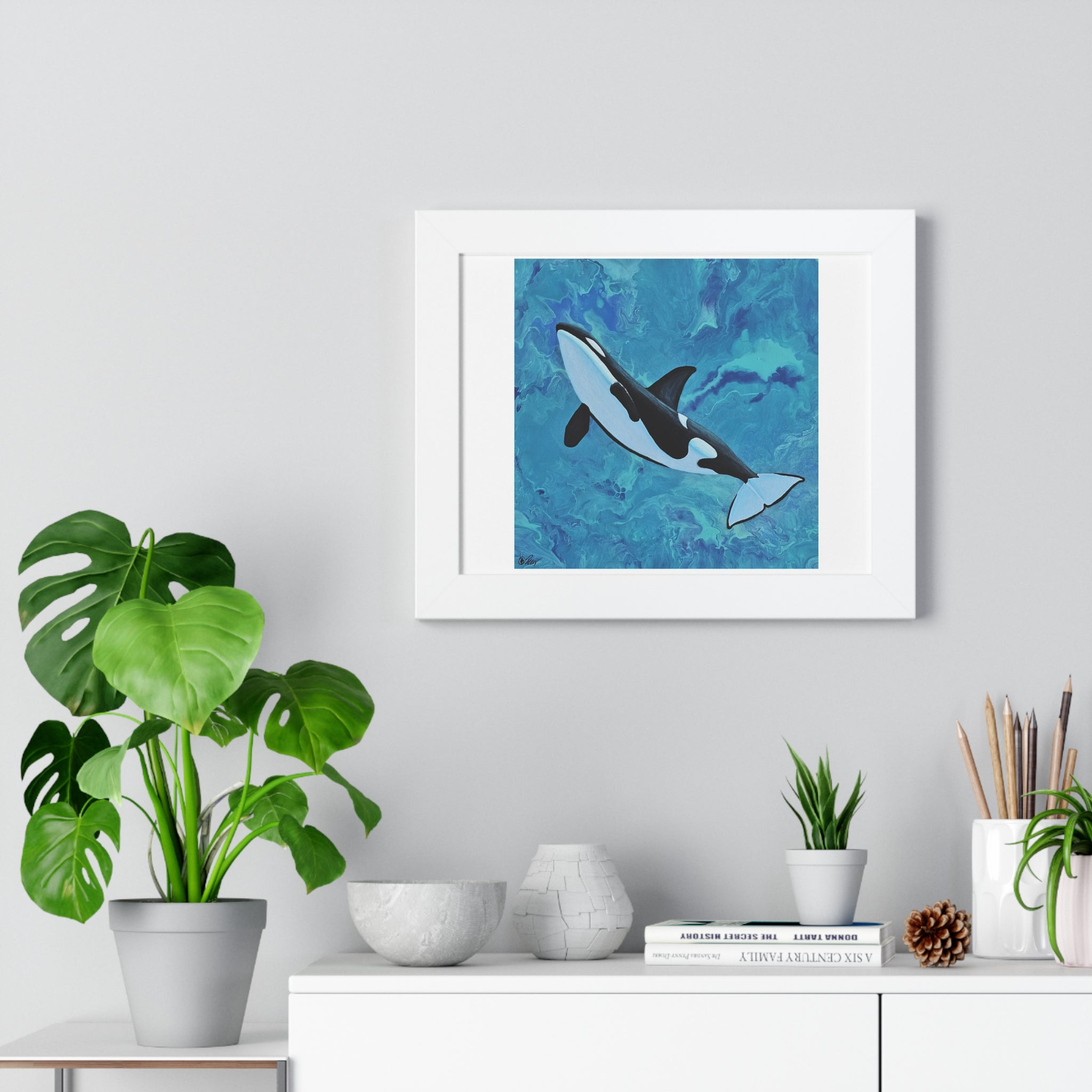 Framed artwork of an orca whale on a wall above a white cabinet with decorative items.