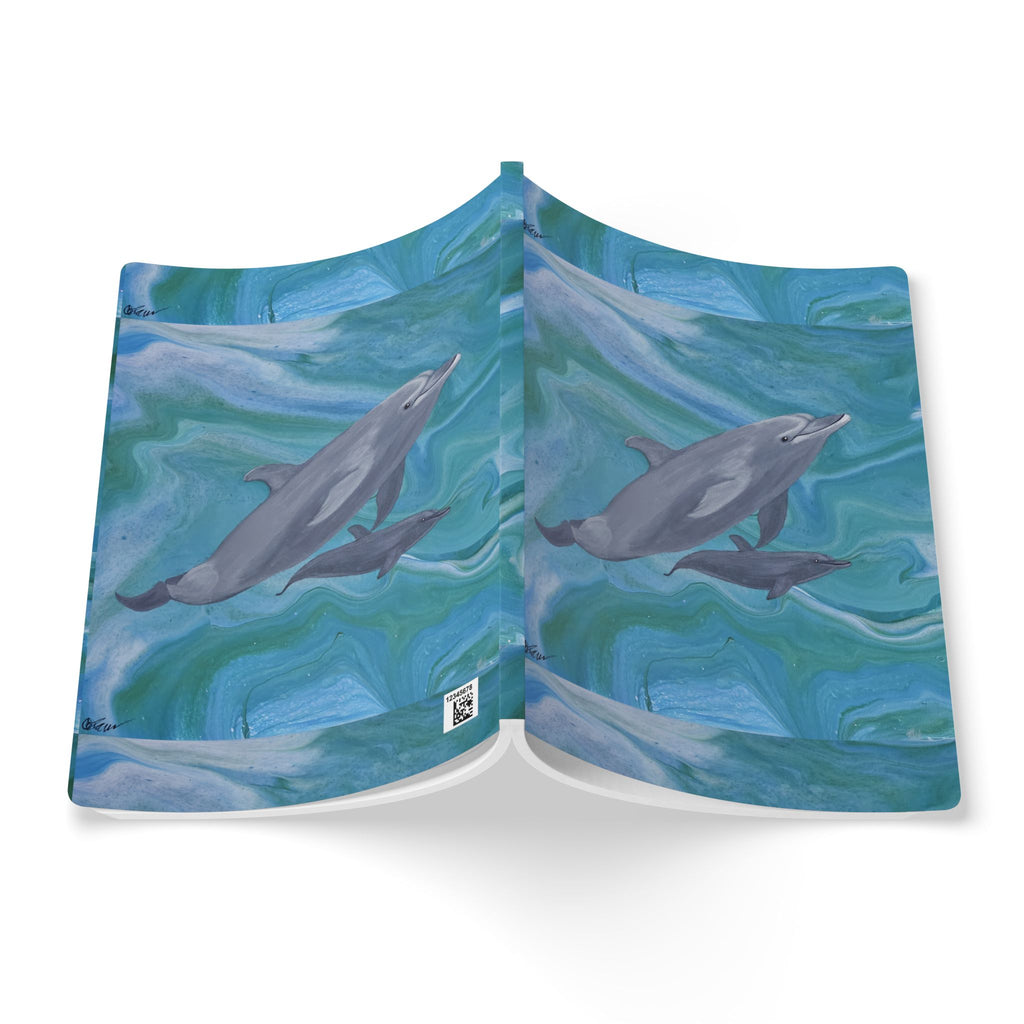 Open notebook with dolphin designs on a blue and green watercolor background.