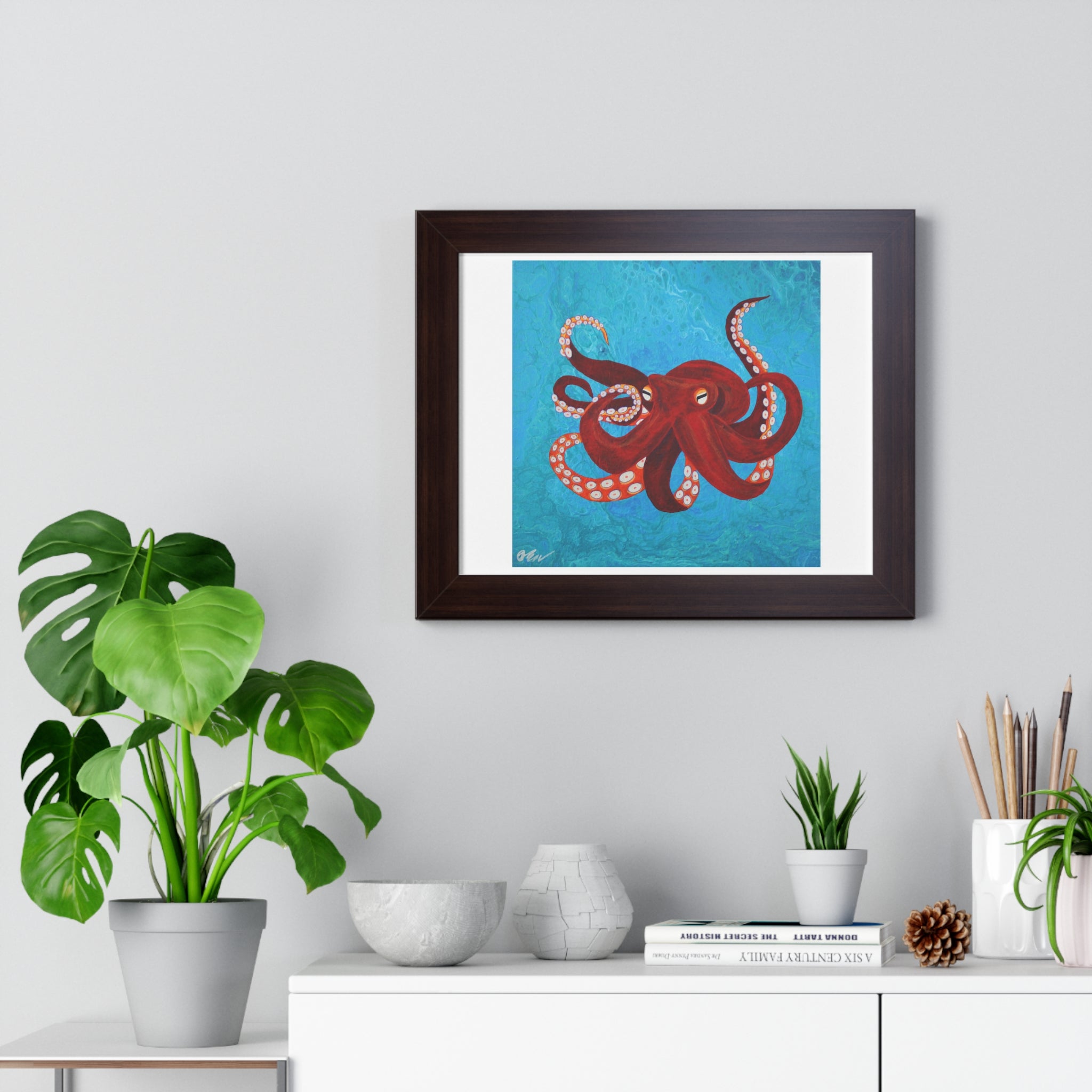 Framed artwork of a red octopus on a blue background, displayed in a room with plants and decor.