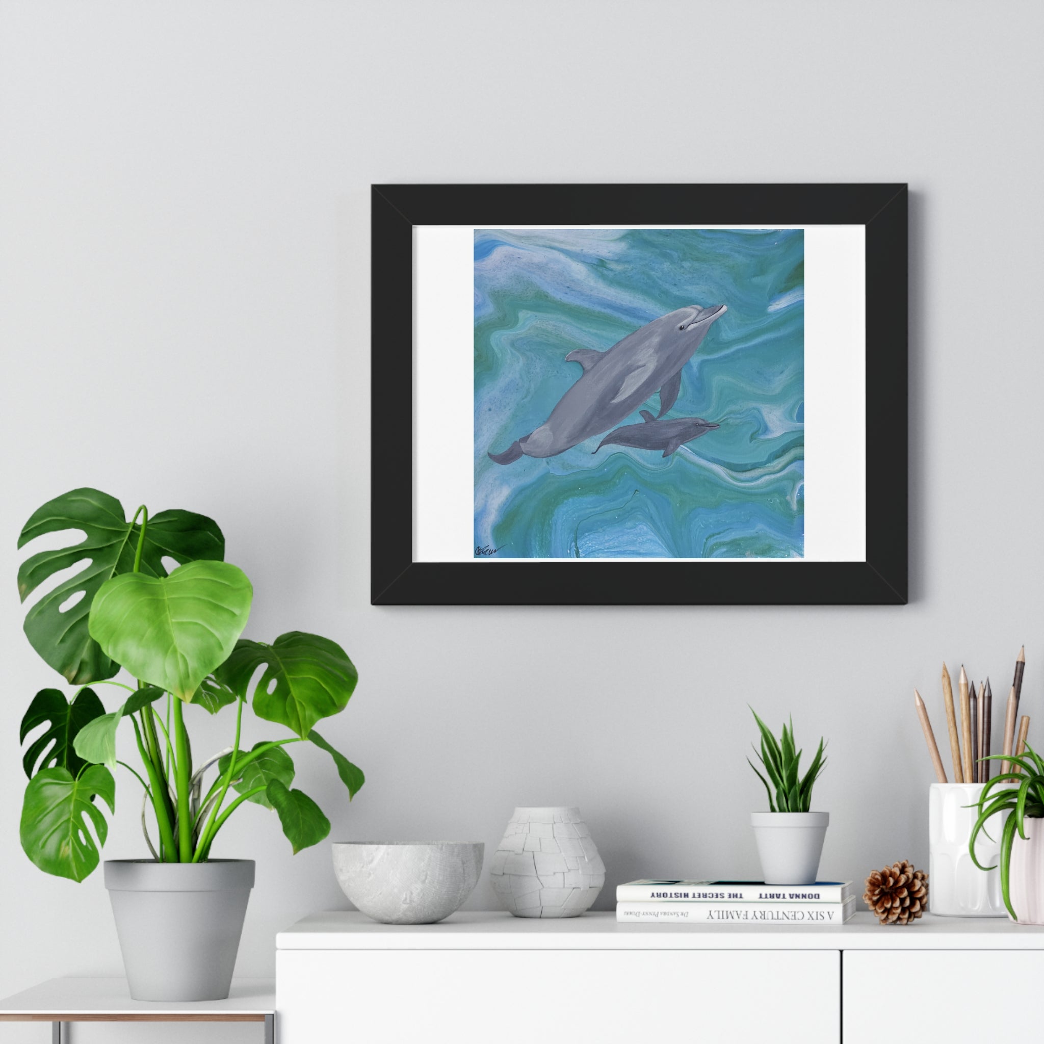 Framed artwork of dolphins on a wall above a white cabinet with decorative items.