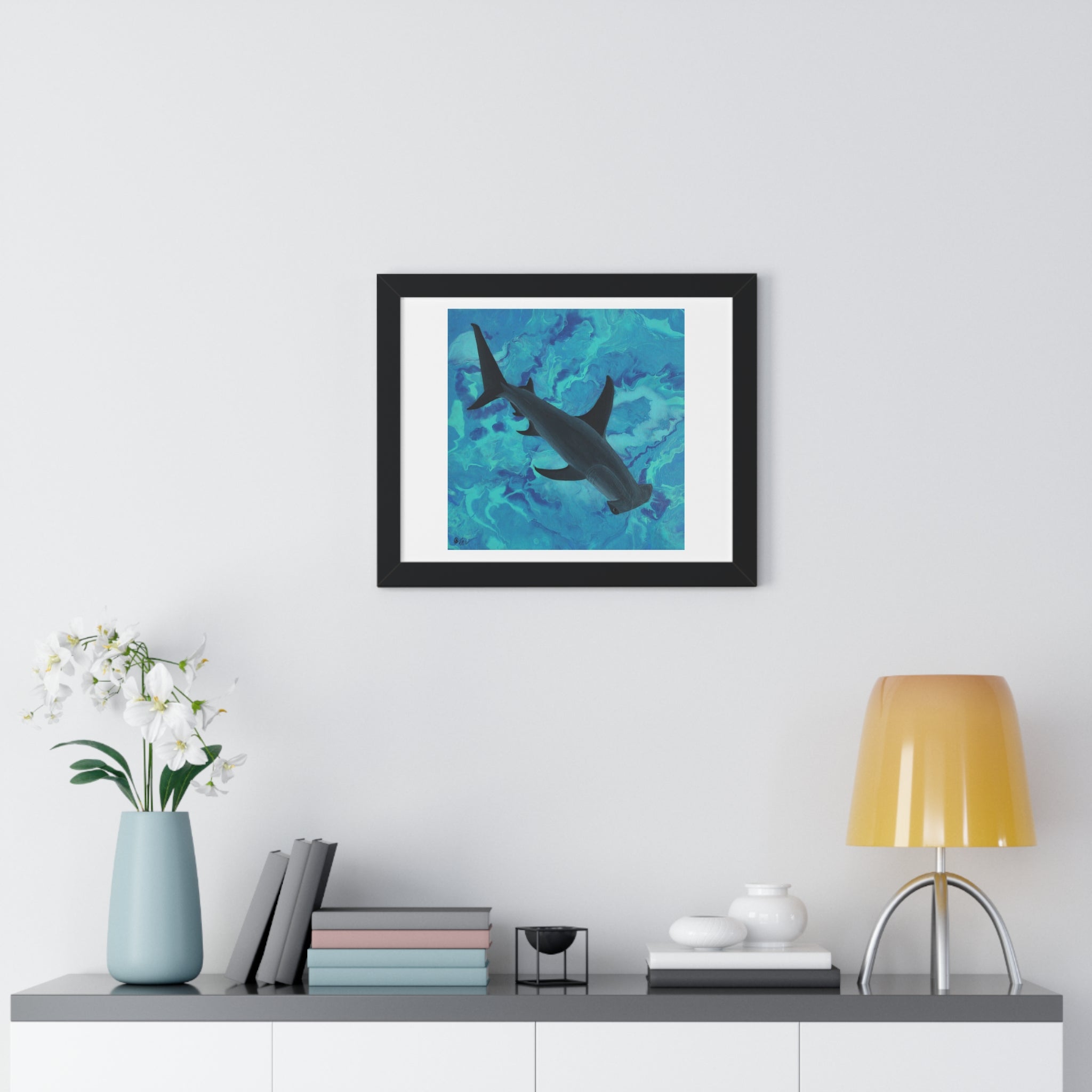 Framed artwork of a shark in water on a wall above a shelf with decor items.