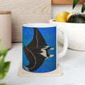 Mug with a manta ray design on a coaster, placed on a surface with a plant and container in the background.