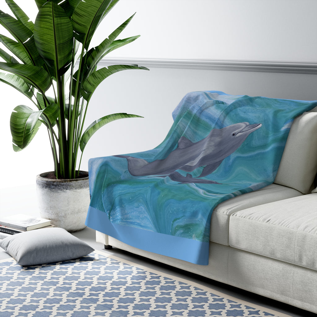 Dolphin-themed blanket draped over a sofa in a living room setting with a plant and rug.