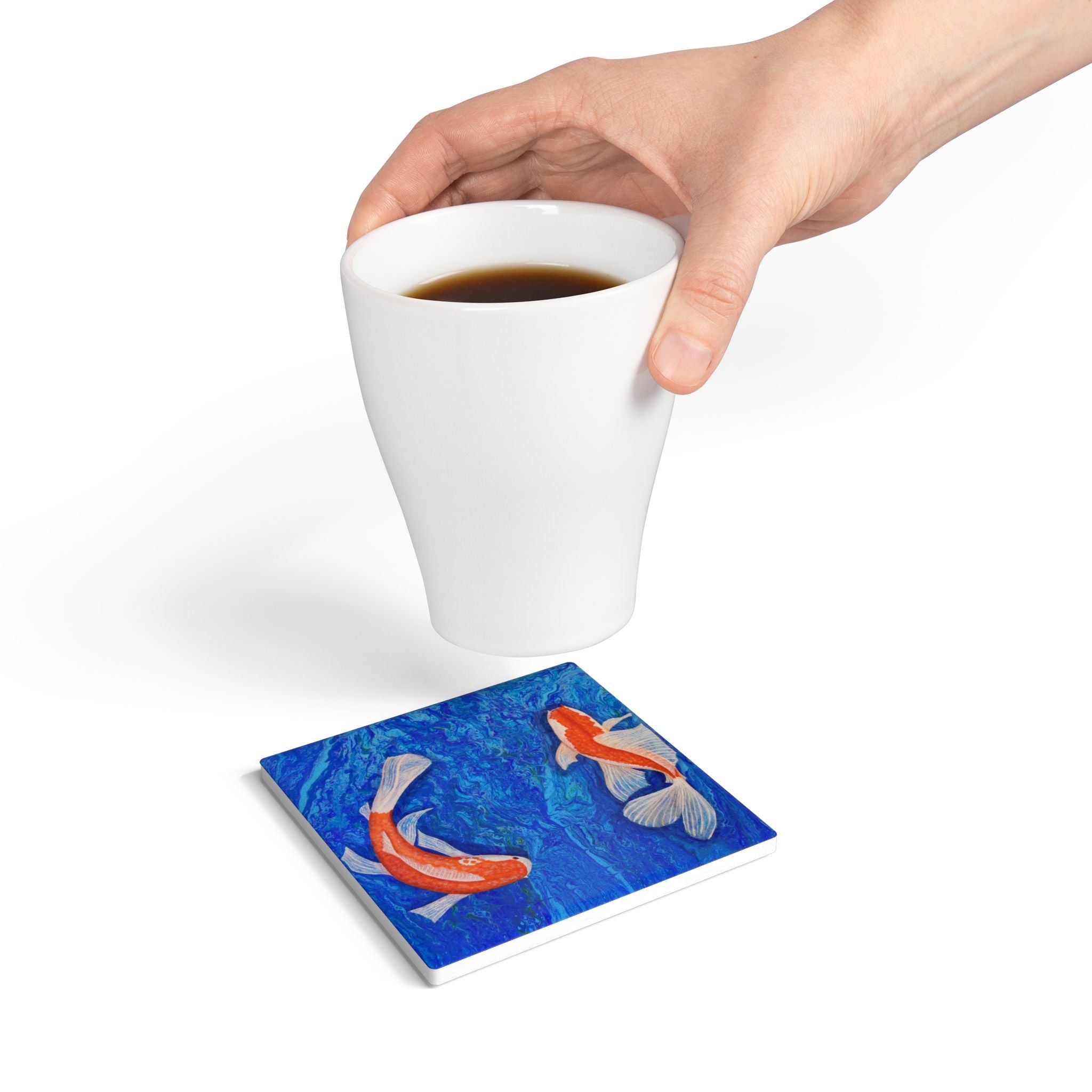 Hand holding a white mug with a blue coaster featuring goldfish design on a white background