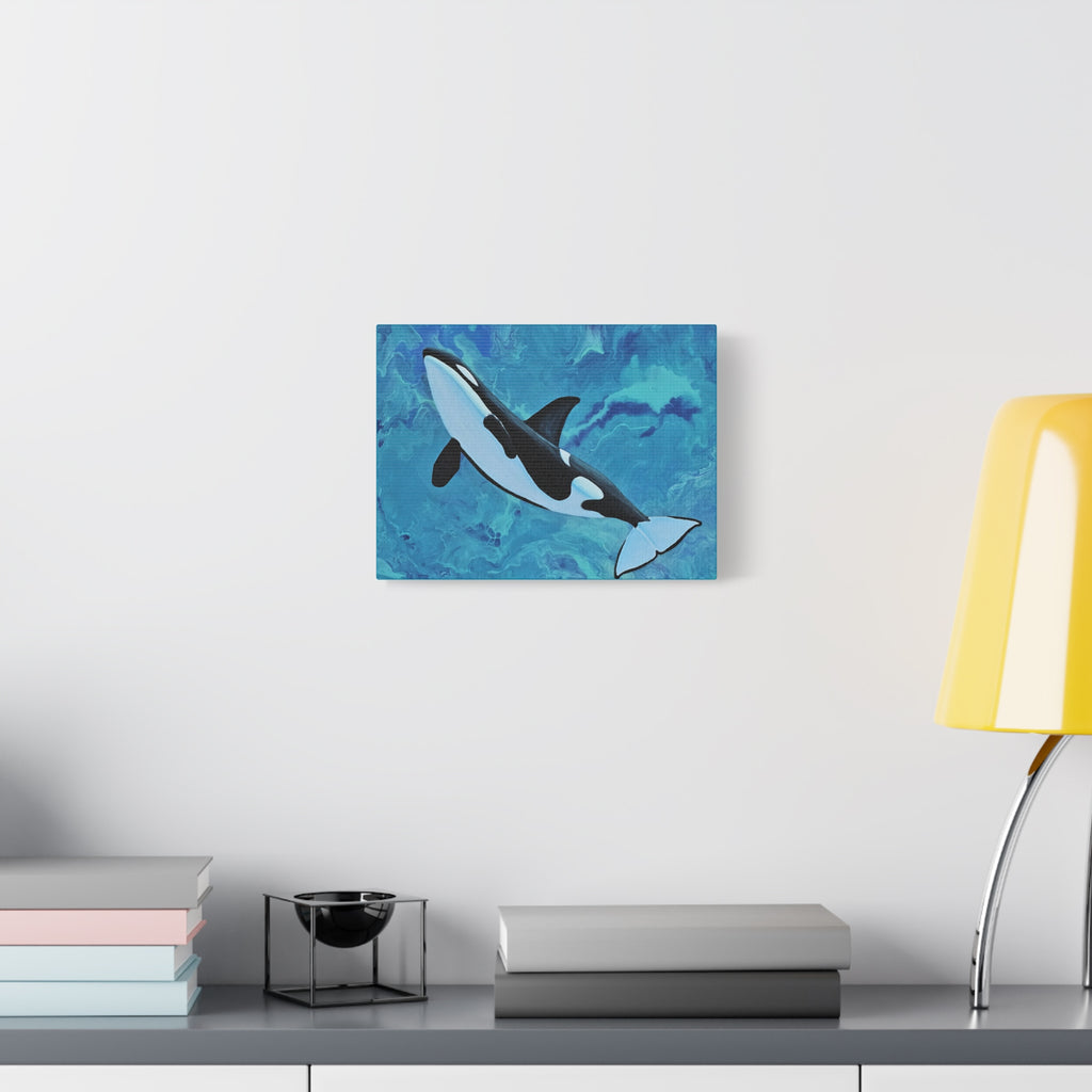 Orca whale painting on a wall above a desk with books and a lamp.