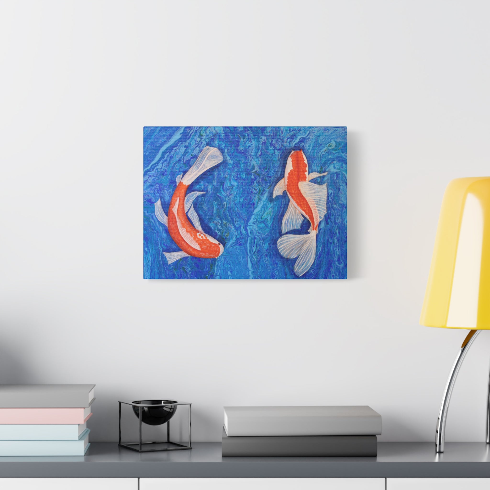 Canvas print of two koi fish on a blue background hanging on a wall above a desk.