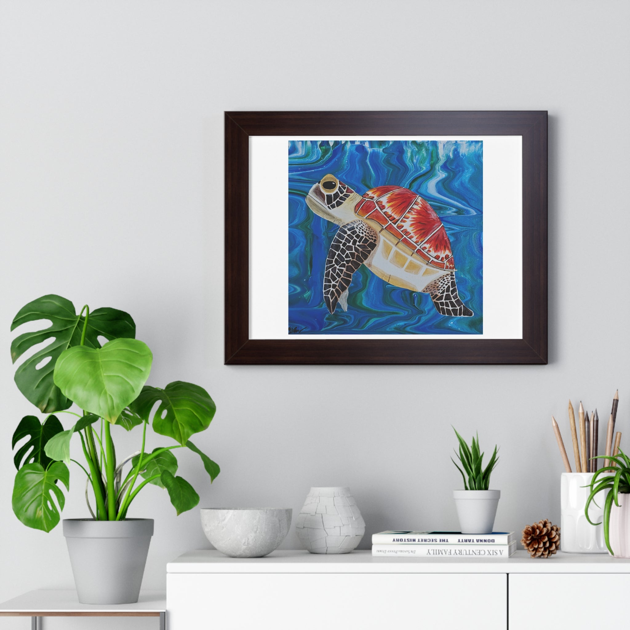 Framed artwork of a turtle on a wall above a white cabinet with decorative items.