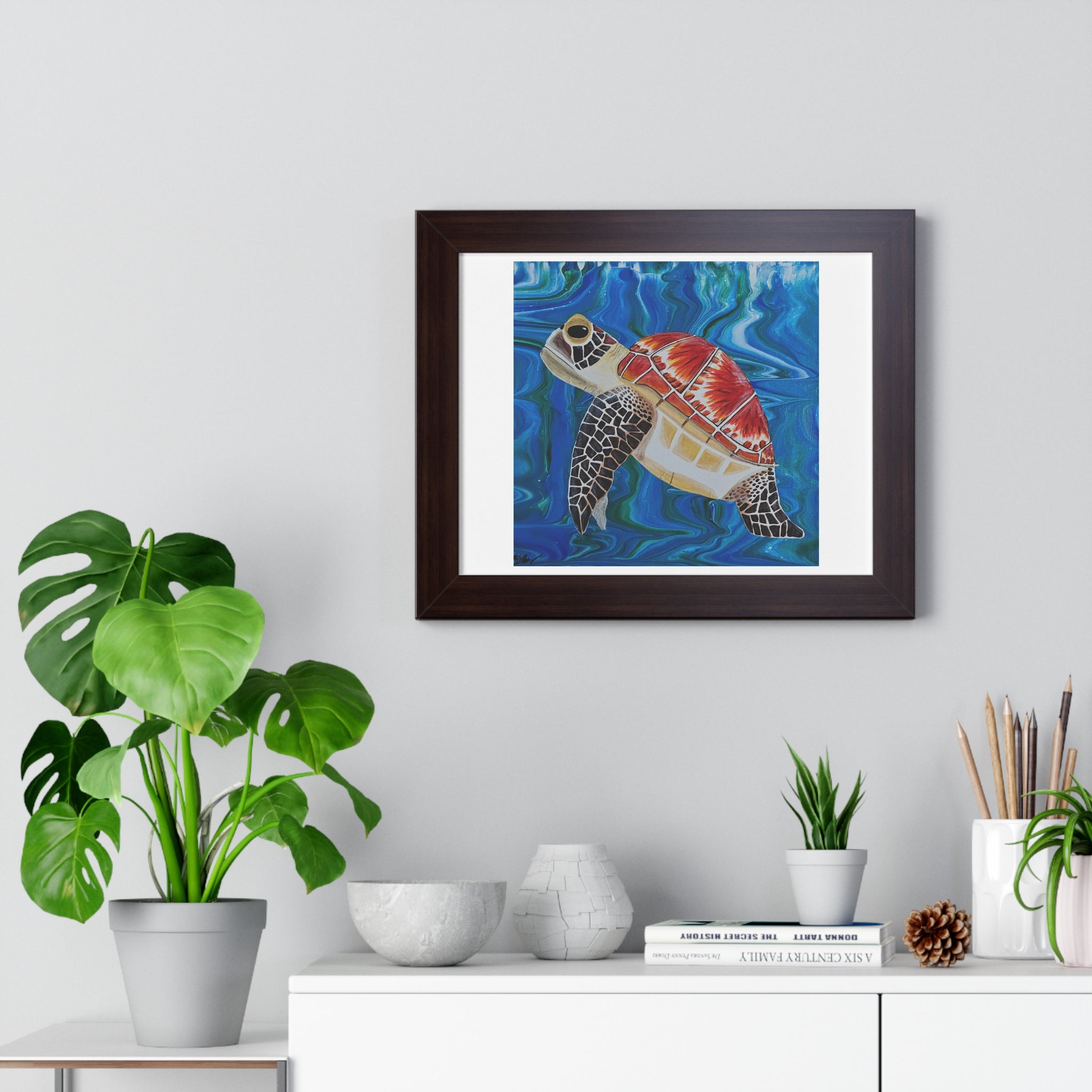 Framed artwork of a turtle on a wall above a white cabinet with decorative items.
