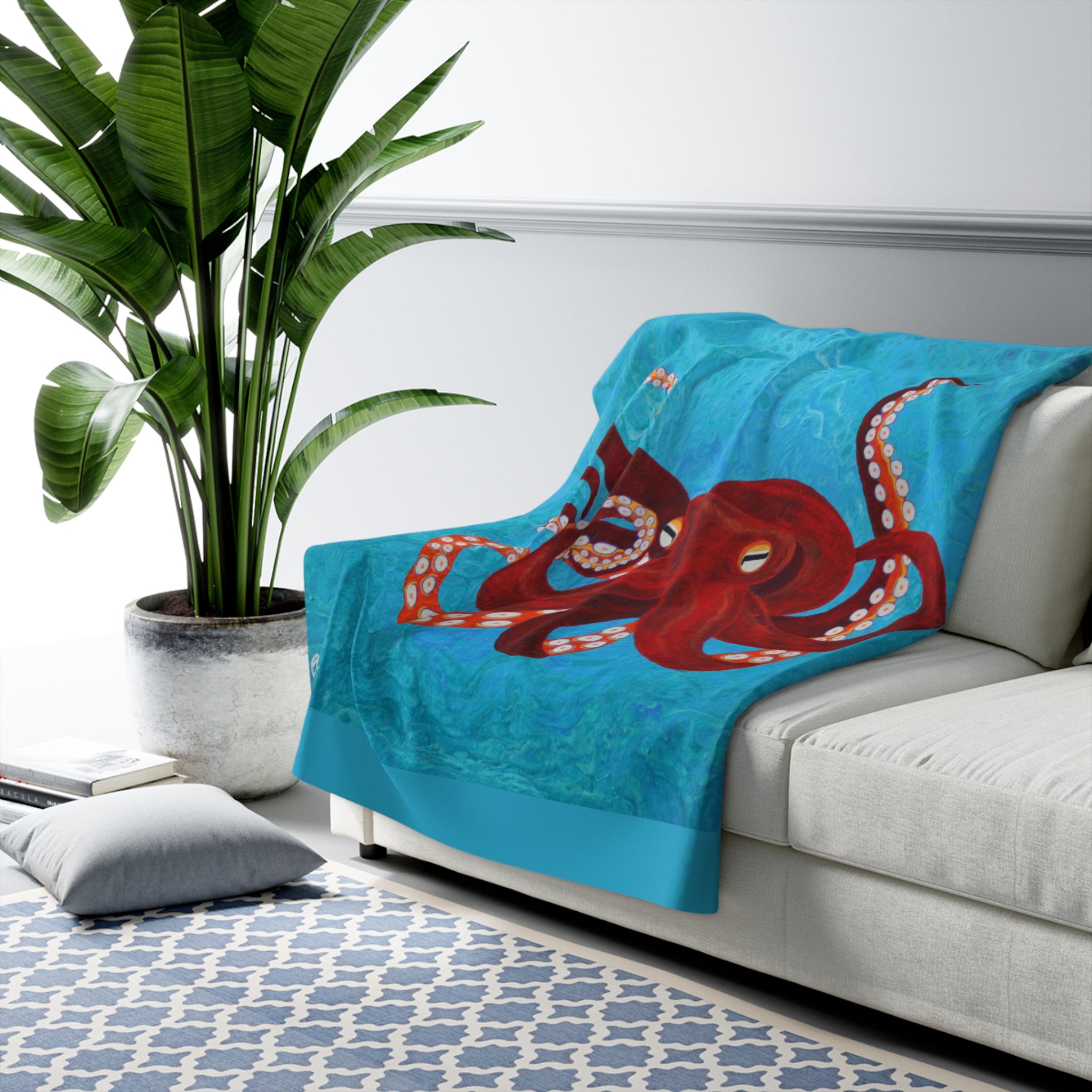 Blue blanket with red octopus design on a white couch, plant and rug in the background