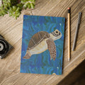 Notebook with a turtle illustration on a wooden surface with stationery items.