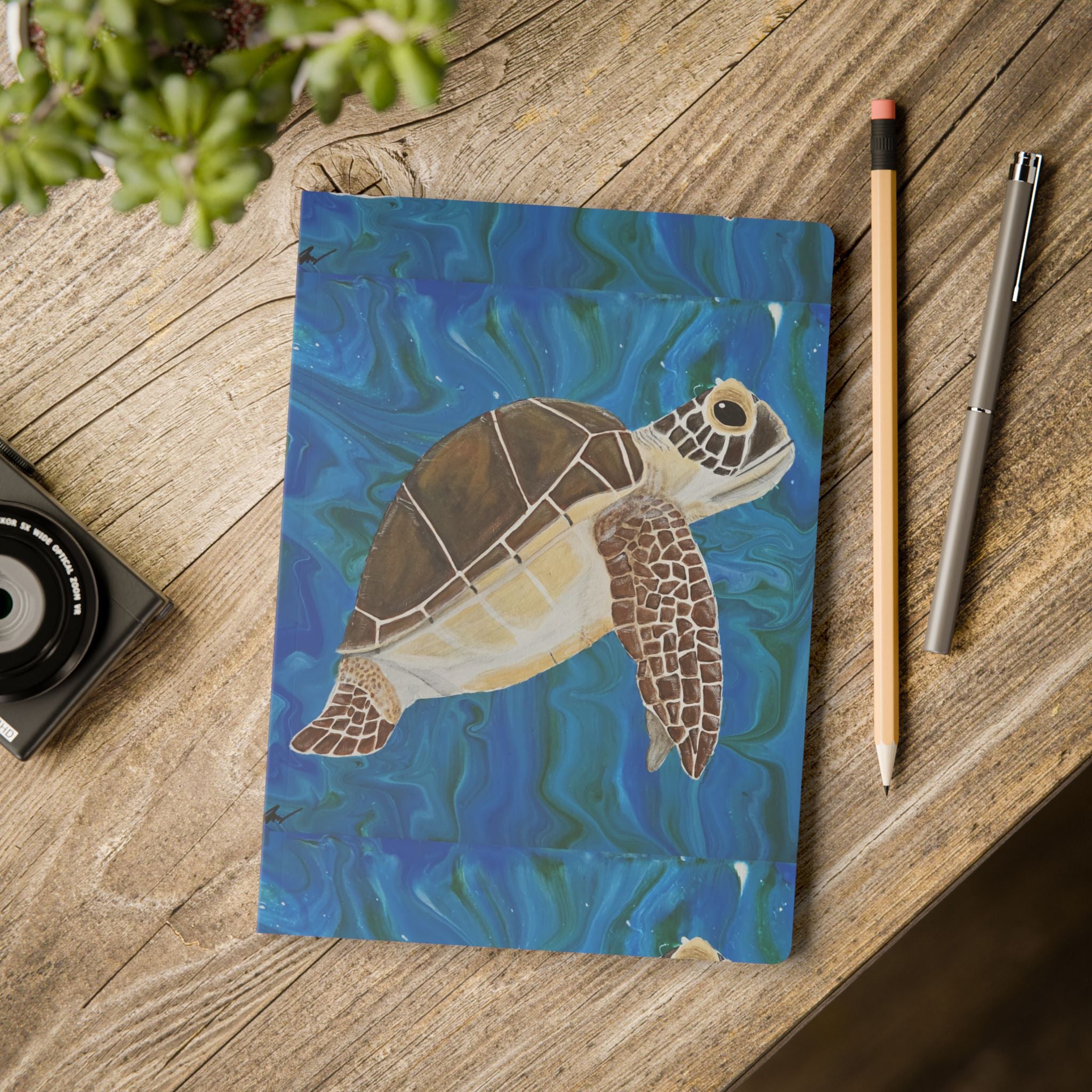 Notebook with a turtle illustration on a wooden surface with stationery items.