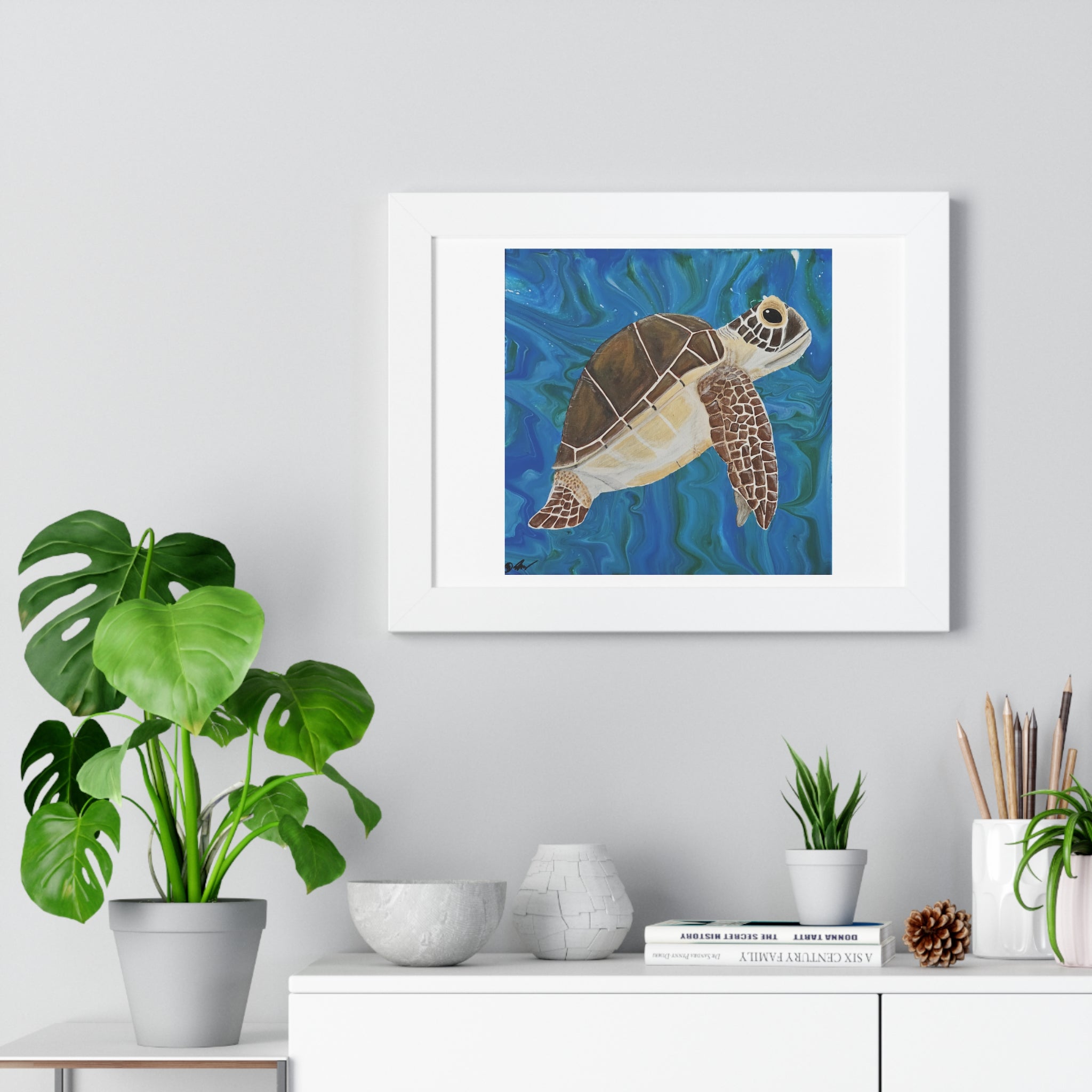 Framed artwork of a turtle on a wall above a white cabinet with plants and decor items.