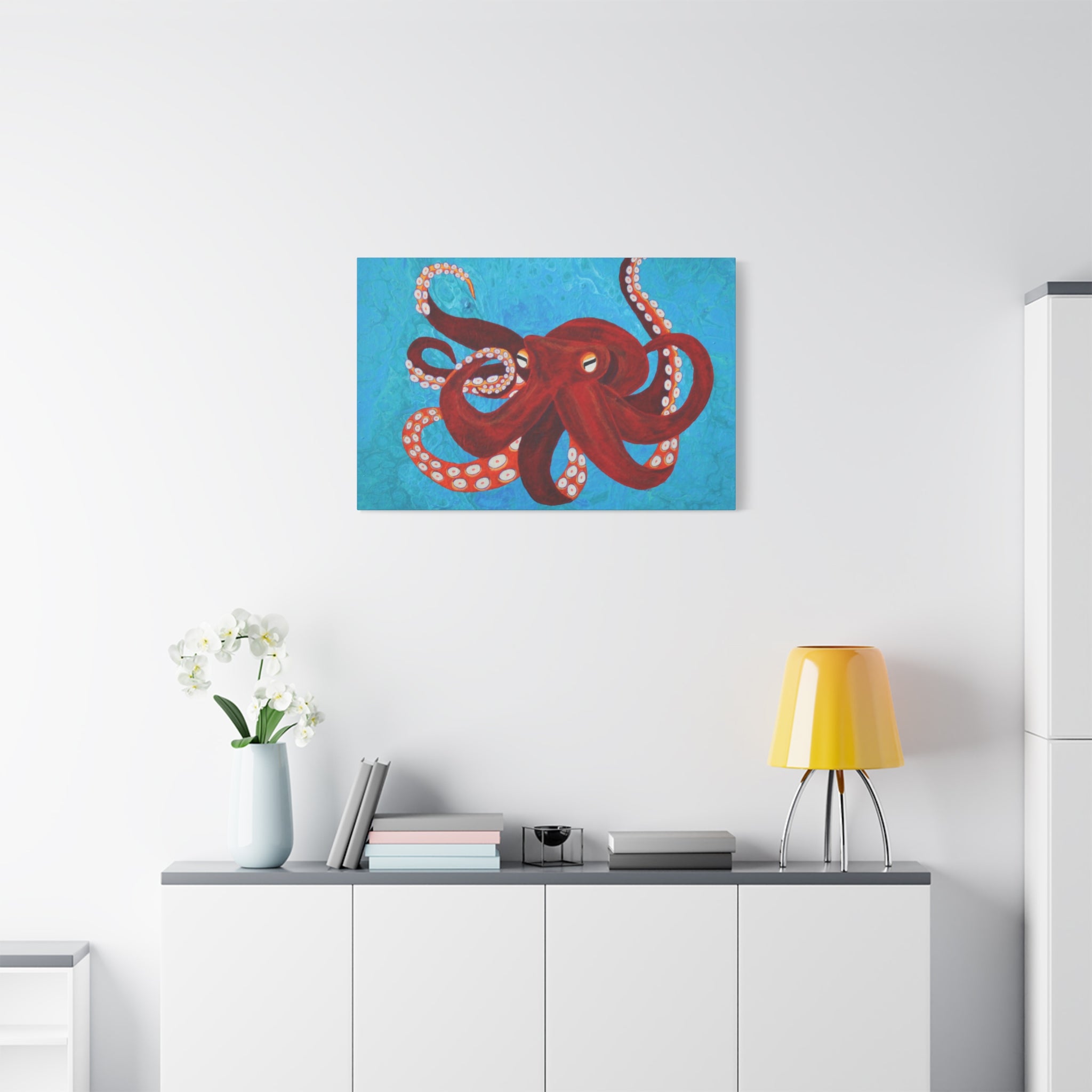 Red octopus painting on a white wall above a white cabinet with a yellow lamp and white flowers.