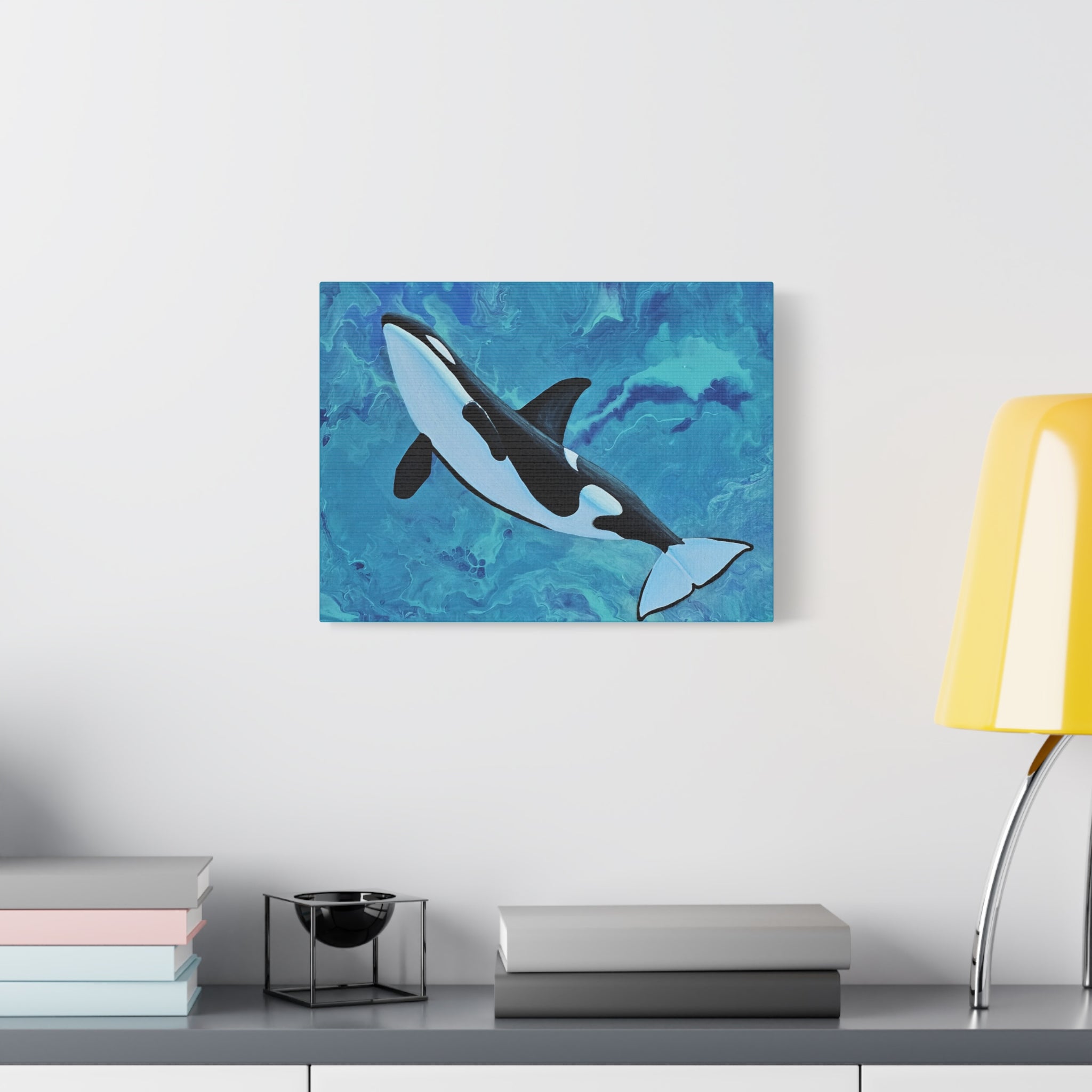 Orca whale painting on a blue abstract background above a desk with books and a lamp.
