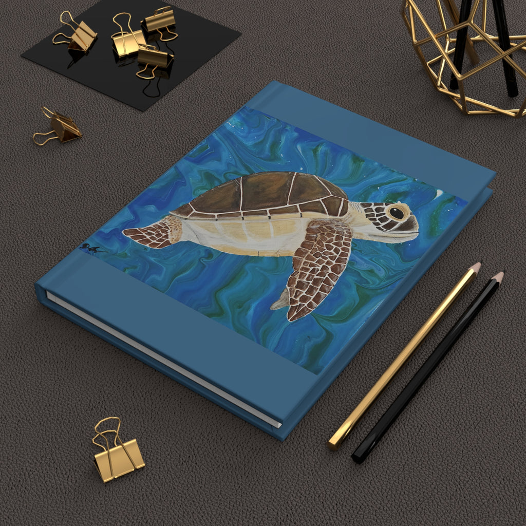 Blue notebook with a turtle illustration on a dark surface with office supplies.