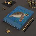 Blue notebook with a turtle illustration on a dark surface with office supplies.