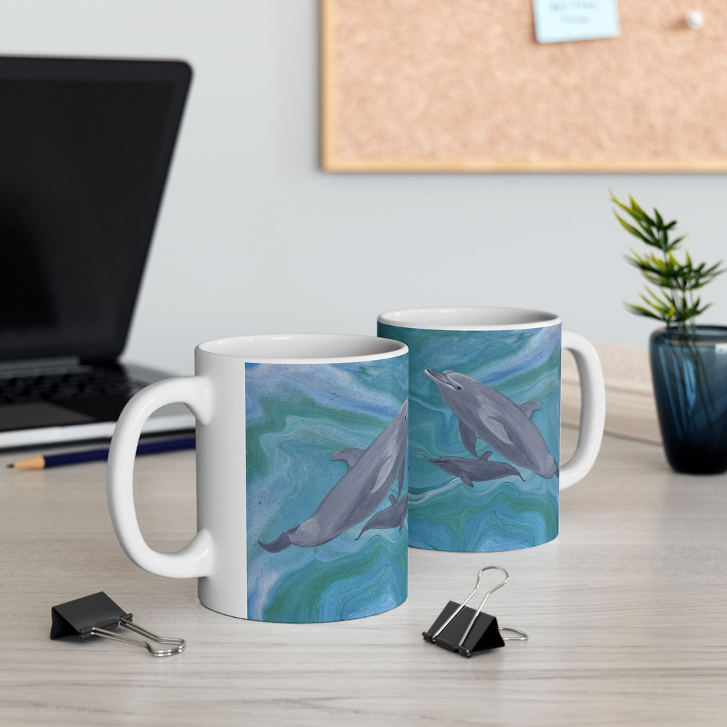 Two mugs with dolphin designs on a desk with office supplies.