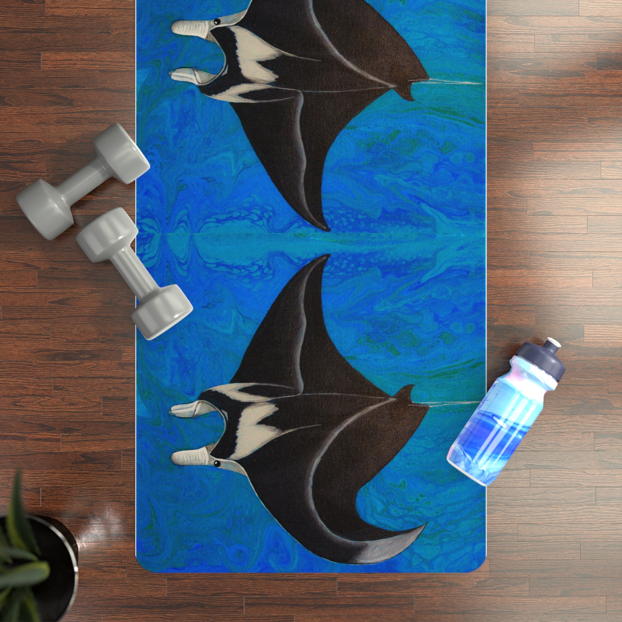 Yoga mat with manta ray design on a wooden floor with dumbbells and a water bottle.