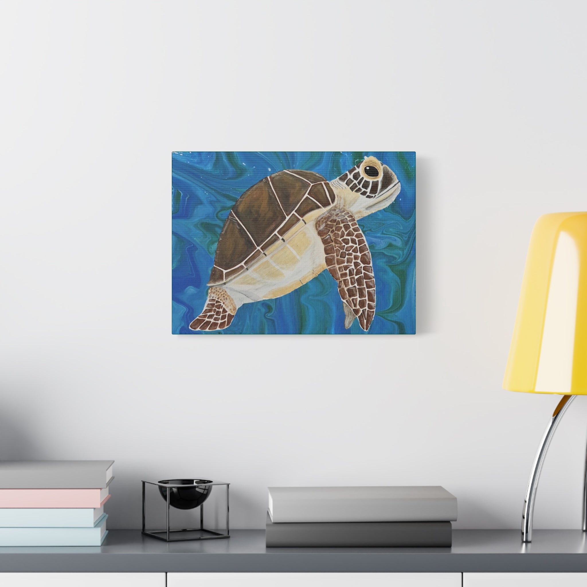 Canvas print of a turtle on a blue background hanging above a desk with books and a lamp.