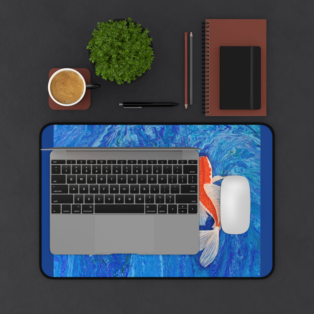 Laptop on a blue koi fish-themed desk pad with office items on a dark surface