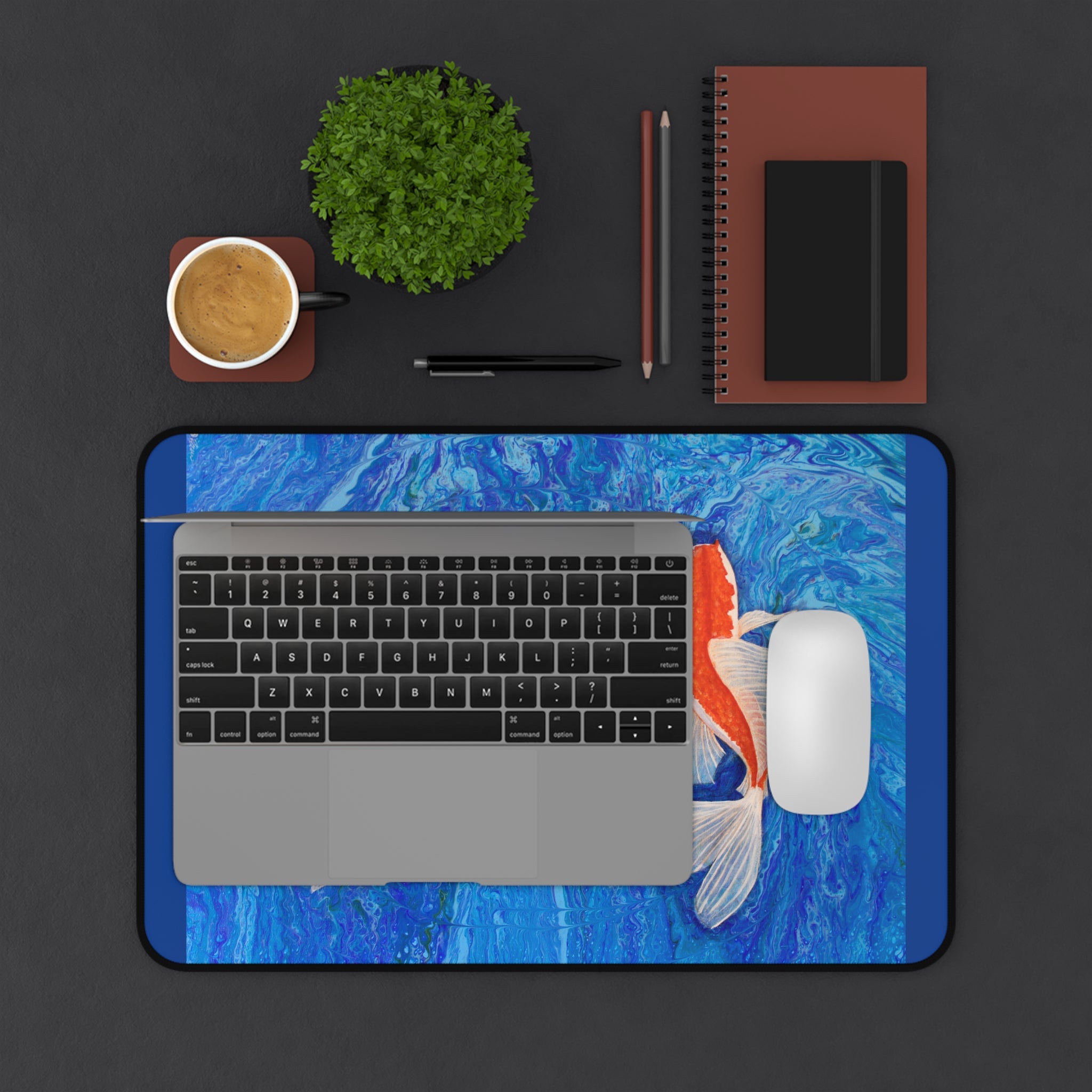 Laptop on a blue koi fish-themed desk pad with office items on a dark surface