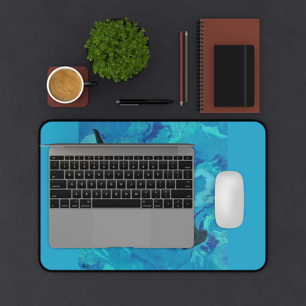Laptop on a blue desk pad with a coffee cup, plant, and stationery items on a dark surface