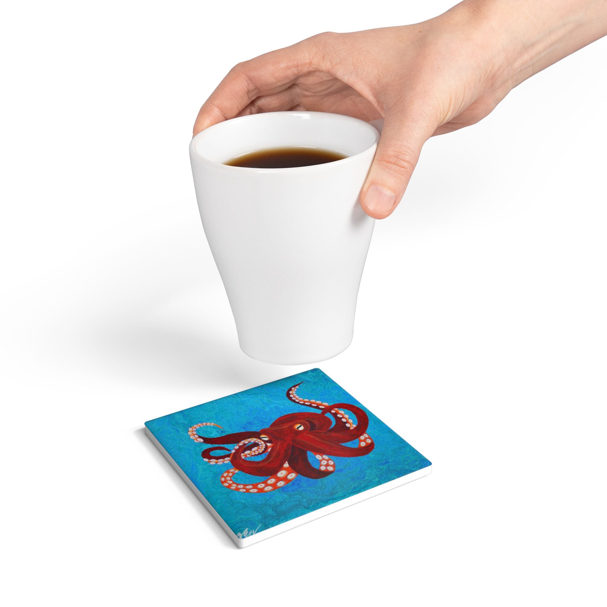 Hand holding a white mug with a blue coaster featuring an octopus design on a white background
