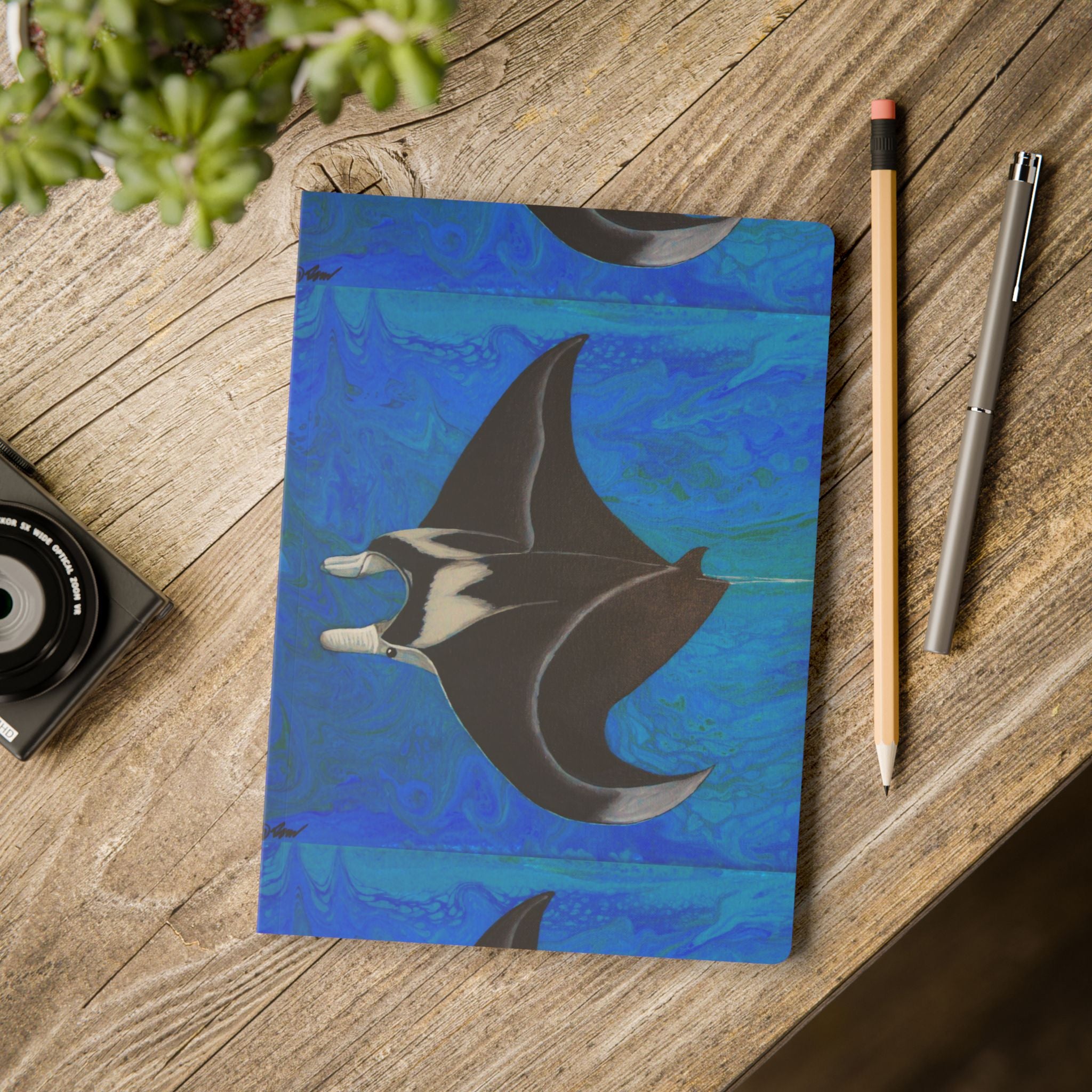 Notebook with manta ray design on a wooden surface with stationery items.