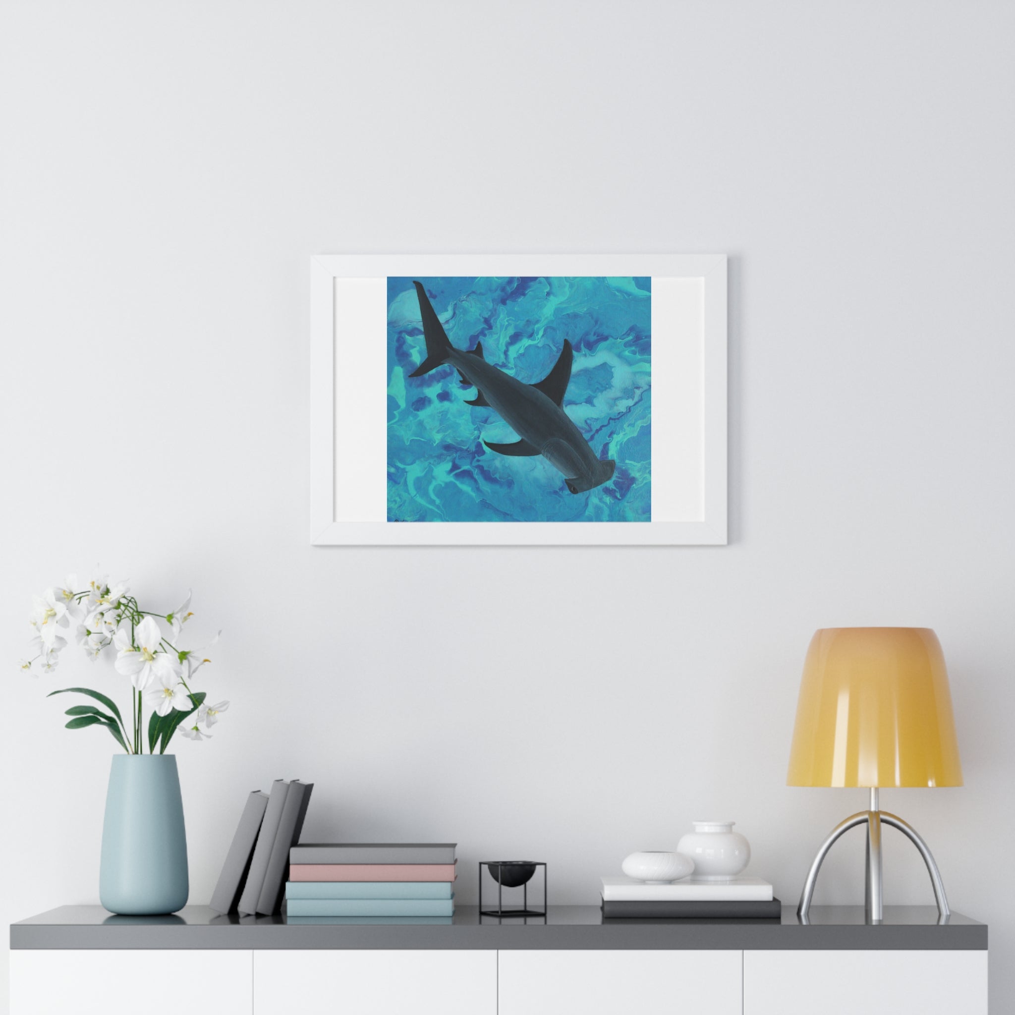 Framed artwork of a shark in water on a wall above a shelf with decor items.