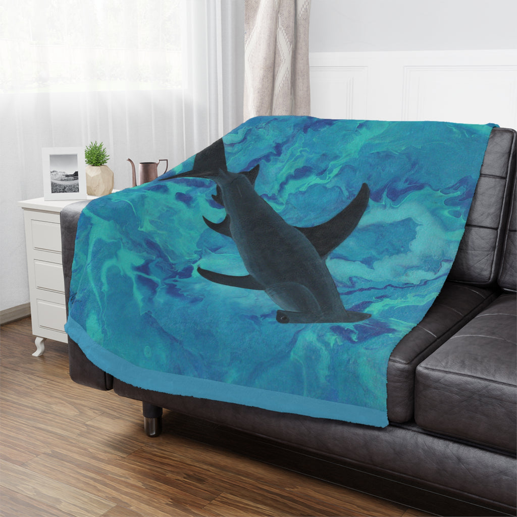 Blue blanket with a hammerhead shark design draped over a black sofa in a room.