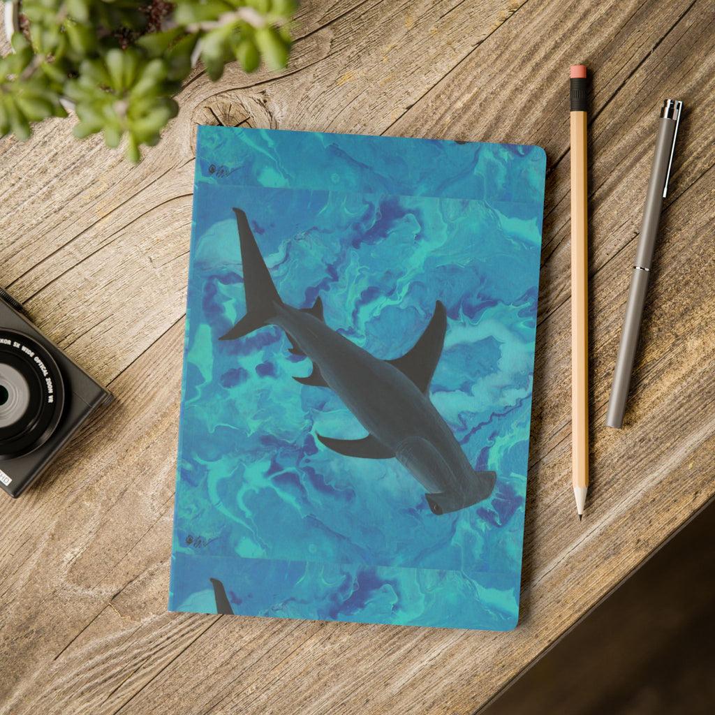 Notebook with shark design on a wooden surface with stationery items