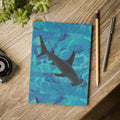 Notebook with shark design on a wooden surface with stationery items