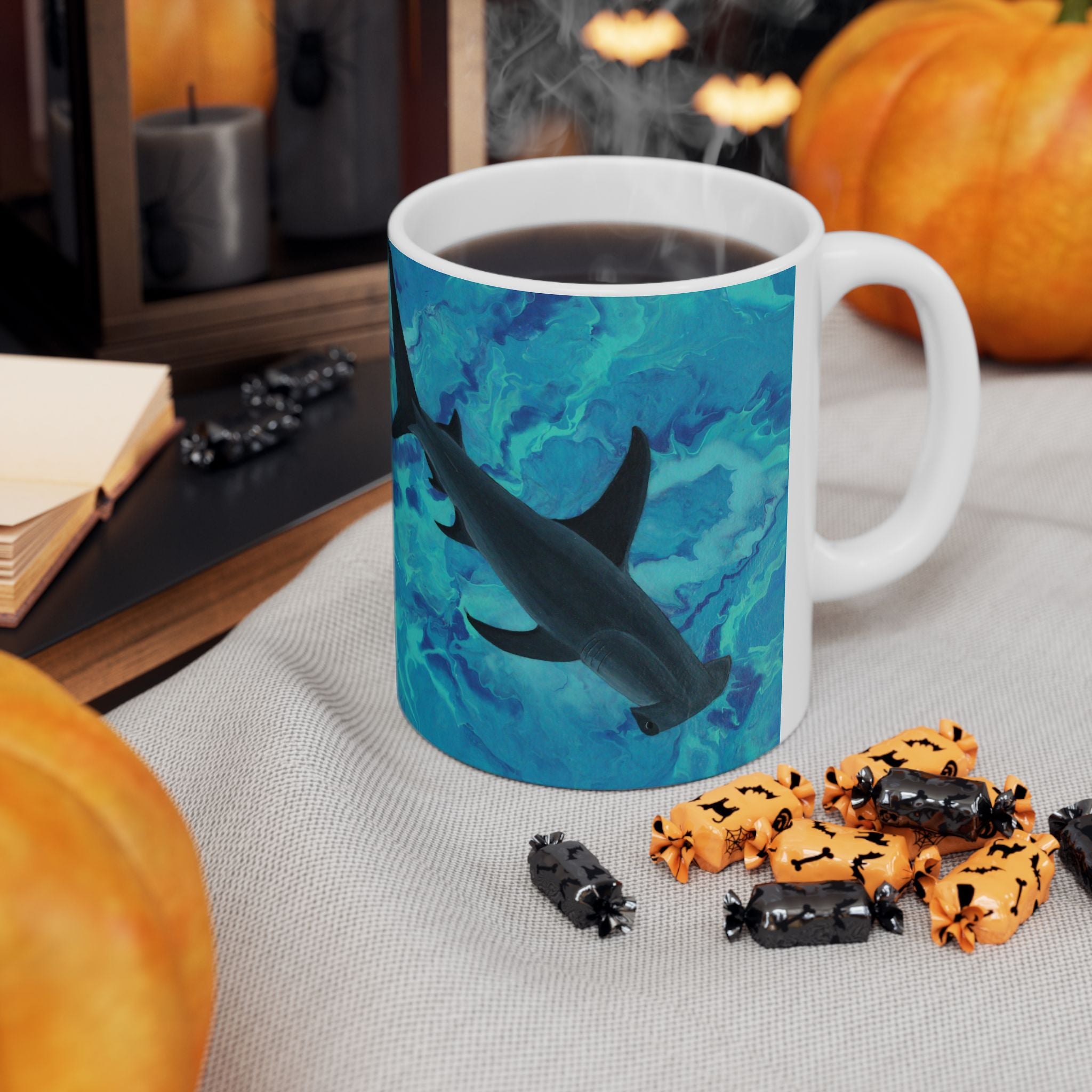 Mug with shark design on a table with Halloween-themed treats and pumpkins.