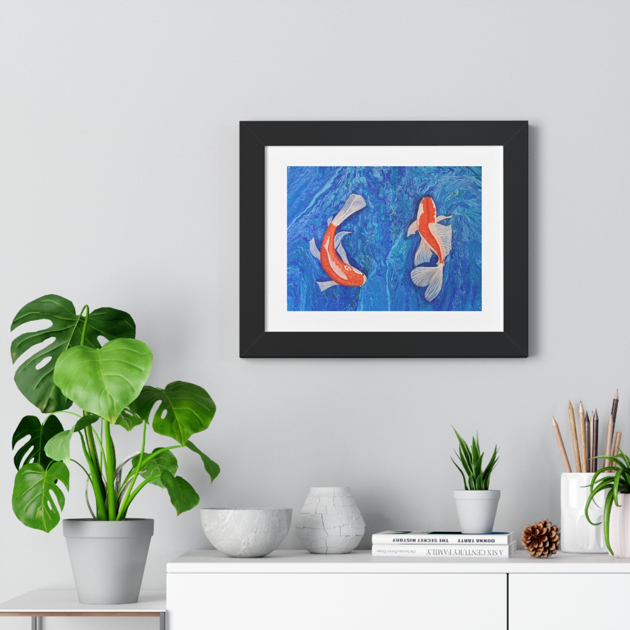 Framed artwork of two fish on a wall above a white cabinet with decorative items.