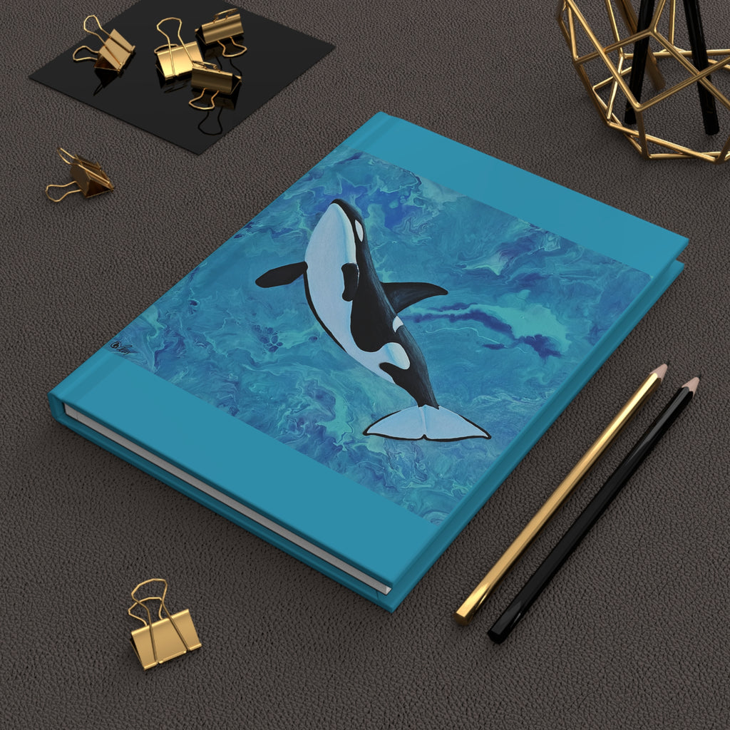 Notebook with an orca whale design on a dark surface with stationery items.